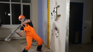 Yıkım işi ve yeniden düzenleme konsepti. Üniformalı ve solunum cihazlı bir erkek balyozla iç duvarı yok ediyor. Yeni dairede yavaş çekimde yeniden geliştirme. Tam Hd