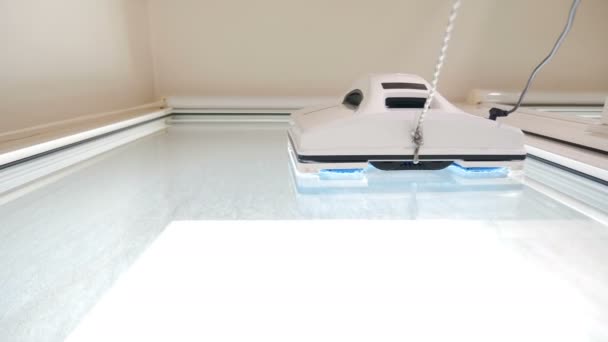 Raamreinigingsrobot aan het werk. Huishoudservice en schoonmaakconcept. Kleine witte robot glaswasser bewegend en draaiend op ramen van appartement close-up. Moderne slimme ruitenwissers. 4k — Stockvideo
