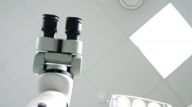 Tedavi için mikroskop aletleri olan modern diş kliniği. Diş mikroskobu beyaz dişçi dolabında, düşük açılı. Kadın dişçi lambayı hafif hastaya çeviriyor. Bakış açısı. 4k video