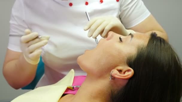 La dentista ortodoncista examina los dientes del paciente en la silla dental, procedimiento dental en la clínica. , primer plano. Estomatólogo sosteniendo herramientas médicas. Paciente femenina de mediana edad en un consultorio odontológico moderno. 4. — Vídeo de stock