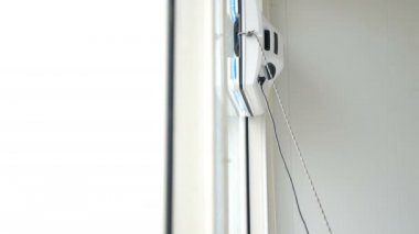 Concept of cleaning service. Small white robot glass washer moving and rotating on windows of apartment, close-up. Modern smart window cleaners. 4k footage