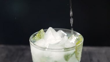 Barmen kokteyl yapar, şeffaf bardağa buz küpleriyle soda döker. Ağır çekim. Siyah zemin üzerinde cam havalanan su. Kokteyl partisi, gece hayatı ve gece kulübü. Tam Hd