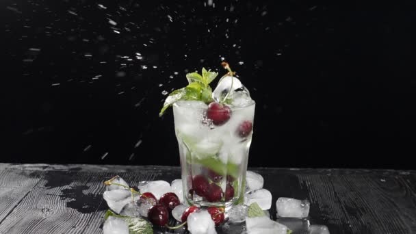 Baya de cereza roja cayendo en cóctel dulce con salpicaduras en cámara lenta. Cantinero haciendo cóctel en vidrio transparente con cubitos de hielo. Agua aireada En vidrio sobre fondo negro. Full hd — Vídeos de Stock