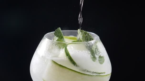 Bartendern gör uppfriskande cocktaillemonad med is, gurka, citron. bubblor som rinner upp i glas i slow motion, närbild. Skjuten på träskiva och svart bakgrund. Fullständig hd — Stockvideo