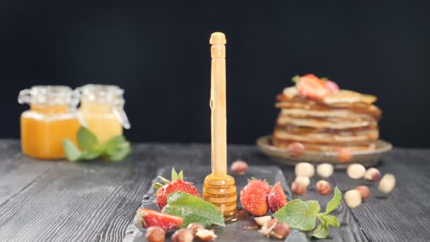 Filmati di cibo al rallentatore. Bastone di legno con miele con miele in vaso di vetro e pila di frittelle in sottofondo. Nocciole che cadono e rotolano. Cibo volante. hd completo — Video Stock