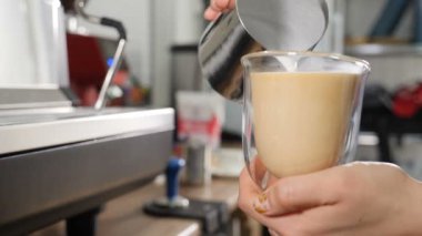Kahve hazırlama süreci. Barista kahve pişiriyor ve şeffaf kupaya taze ve kalın süt döküyor. Kahveci Latte yapmak için süt dökerken yakın çekim. Ağır çekim. Tam Hd