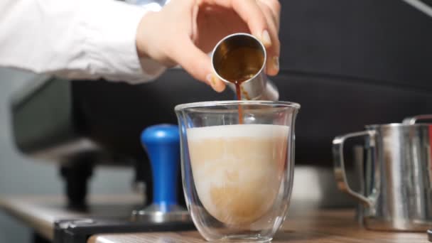 Warme melk in een kop espresso gieten, slow motion. Barista aan het werk. Koffie mengen met room. Lekkere witte melk die langzaam uit zilveren kruik in een kopje bruine schuimkoffie stroomt. Vol hd — Stockvideo