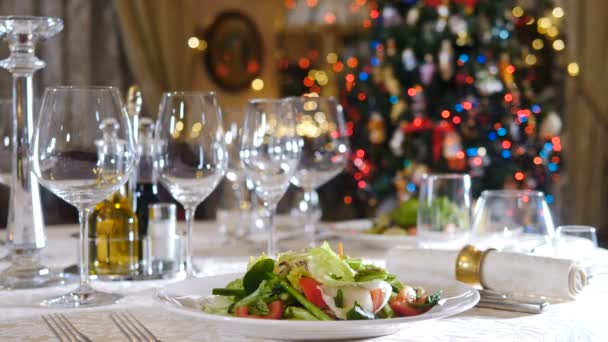 Τραπέζι διακοπών σερβιρισμένο για Χριστουγεννιάτικο δείπνο στο σαλόνι. Χειμερινό τραπέζι διακοπών σερβίρεται, Πρωτοχρονιά δέντρο αναβοσβήνει. Σαλάτα λαχανικών στο τραπέζι. Διακόσμηση διακοπών. Σχέδιο εστιατορίου. 4 k βίντεο — Αρχείο Βίντεο