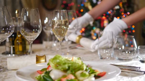レストランのコンセプト。新年とメリークリスマスのごちそうテーブル。背景にテーブルの上にナプキンを置く手袋でウェイター。ホリデーツリーライトが点滅します。お祝いに美しく振舞われる料理やグラス — ストック動画