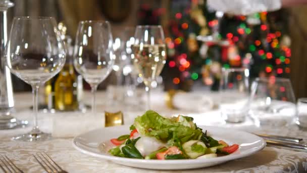 Conceito de restaurante. Ano Novo e mesa de festa de Feliz Natal. Garçom em luvas colocando copo de vinho na mesa no fundo. luzes da árvore de férias piscando. pratos servidos na mesa de celebração. 4 k — Vídeo de Stock