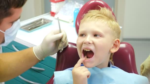 Dental health concept. Male dentist treating little boy in dental clinic. Pediatric dentistry. Dentist examines teeth of boy holding medical tools. 4 k footage — Stock Video