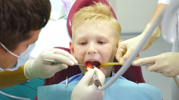 Concepto odontológico. Niño paciente sentado en la silla dental en el consultorio de dentistas pediátricos. Asistente y dentista masculino trabajando juntos. Primer plano del paciente de Boy en la clínica dental recibiendo tratamiento. 4. — Vídeo de stock