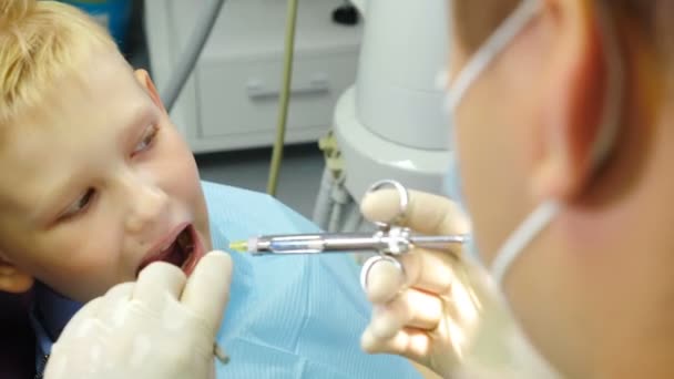 Conceito de Odontologia. Paciente infantil sentado em cadeira dentária em consultório de dentistas pediátricos. tiro de perto de paciente menino na clínica dentária recebendo injeção de anestésico. 4 k vídeo — Vídeo de Stock