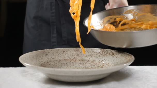 Close-up shot van mannelijke chef-kok zet afgewerkte spaghetti pasta van pan op bord in restaurant keuken. Voedselingrediënt. Goed gekookt. Het bereiden van voedsel video. Langzame beweging. Vol hd — Stockvideo