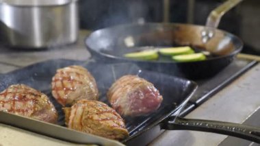 Restoranda yemek pişirmek. Izgara tavada biftek. Şef biftek yapıyor. Izgarada pişen lezzetli etli biftekler. 4k görüntü