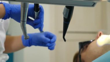 Diş tedavisi prosedürü. Diş muayenehanesinde gözlüklü erkek hasta, yakın plan. Çalışırken dişçi aleti. Stomatoloji kliniğinde dişçi seansı. Hastalıklı dişlerin tedavisi. 4 bin.