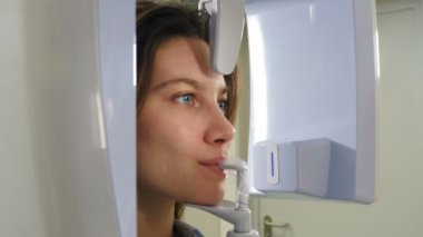 Genç gülümseyen kadın hasta ortomografi makinesi kullanarak ağız boşluğunda panoramik röntgen çekiliyor. Yakın plan çekim. Modern diş kliniğinde tomografi tarayıcısı. 4k video