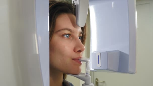 Genç gülümseyen kadın hasta ortomografi makinesi kullanarak ağız boşluğunda panoramik röntgen çekiliyor. Yakın plan çekim. Modern diş kliniğinde tomografi tarayıcısı. 4k video — Stok video