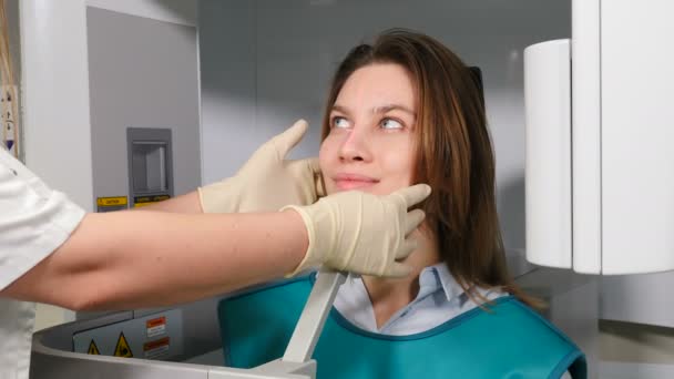 Médico radiólogo en clínica dental ajustando la cabeza del paciente femenino antes del procedimiento de RMN. Escaneo dental. Mujer joven agradable que se somete a pruebas en el escáner dental de rayos X. 4 k vídeo — Vídeos de Stock