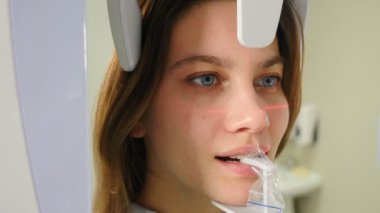 Genç gülümseyen kadın hasta ortomografi makinesi kullanarak ağız boşluğunda panoramik röntgen çekiliyor. Yüzünde lazer izleri var. Modern diş kliniğinde tomografi tarayıcısı. 4k video