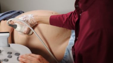 Doktor el, karnındaki güç çevirici jöle ile açılmış. Doktor Ultrason yapıyor, hamile kadına sonogram prosedürü uyguluyor. Yakın plan. Ultrasonografi süreci. 4k video