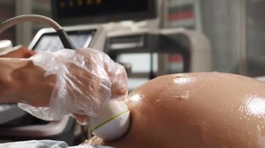 Doktor doğurganlık uzmanı hamile kadını kontrol ederken ultrason cihazı kullanıyor. Hamile kadın ultrason araştırması yaptırıyor. Ultrason ile doğum öncesi testleri. 4k video