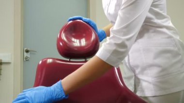 Kadın dişçi asistanının dezenfektan solüsyonuyla tıbbi sandalyeyi silerken yakın çekim. Modern diş kliniğinde sterilizasyon diş hekimliği bölümü, ameliyat tesisi. 4k görüntü
