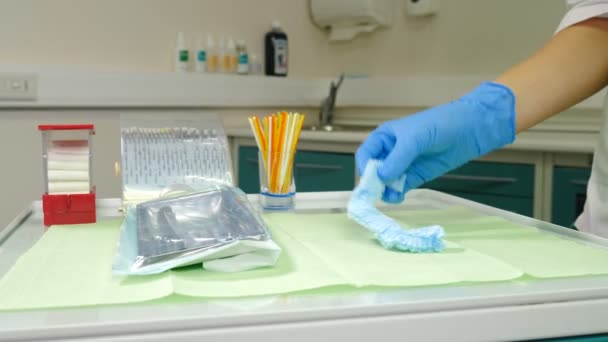 Biuro stomatologiczne w przygotowaniu. Asystent medyczny umieszczający przedmioty dla dentysty do założenia: sterylne rękawiczki, kapelusz i maska na twarz. Przed leczeniem pacjenta. Materiał 4 k — Wideo stockowe