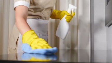 Otelde temizlik. Genç kadın hizmetçiyi apron temizliği yaparken, masa yüzeyini mikrofiber bezle silerken, mavi bez parçasıyla, ahşap masa yüzeyini dikkatlice silerken yakın çekim. 4k video