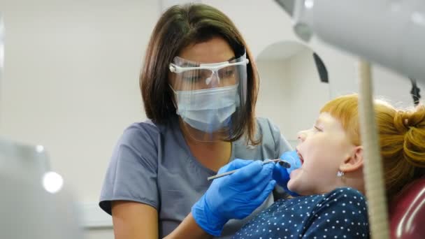 Nowoczesne biuro dentystyczne. Portret kobiety dentysty leczącej rudą dziewczynkę w klinice stomatologicznej. Stomatologia dziecięca. Urocze dziecko w gabinecie dentystycznym. 4 tys. wideo — Wideo stockowe