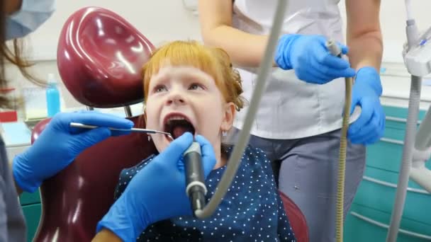 Odontología pediátrica. Un niño encantador en el consultorio del dentista recibiendo tratamiento dental. Dentista y asistente trabajando juntos. Concepto odontológico. 4 k vídeo — Vídeo de stock