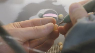 Diş protezi, yapay diş, protez. Dişleriyle yapay çene kalıbı tutan teknisyen diş laboratuarında kumla cilalayan seramik taçlarla çalışıyor. 4k video