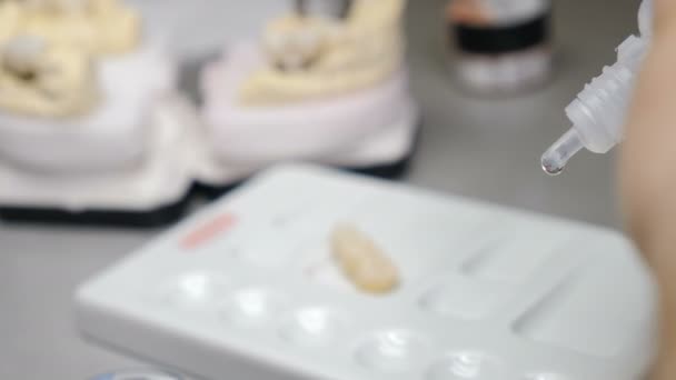 Зубной техник, работающий с керамическими коронками в стоматологической лаборатории. Техник работает над новыми зубными протезами, готовится нанести цвет на цирконий. 4 k видео — стоковое видео