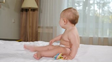 Yatak odasında oynayan, gülümseyen kameraya bakan güzel bir kız. 9 aylık mutlu bebek oyunu. Yatakta oturan güzel bir kızın portresi. Özel evde rahat bir oda. İpotek hizmetlerini karşılama