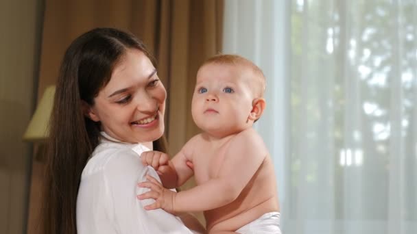 幸せな若い母親は彼女の赤ん坊を見ている。子供、赤ん坊、親、子供時代、人生、産前産後の概念。美しい笑顔の赤ちゃん。4 kビデオ — ストック動画