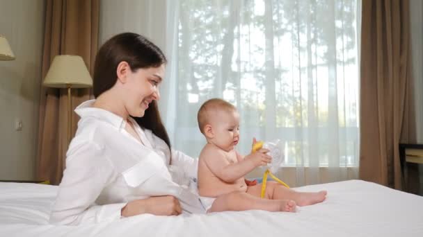 Portret van een aantrekkelijke jonge vrouw met haar schattige kind op bed. Gelukkig zwangerschapsconcept. liefdevolle gelukkige moeder knuffelt 8 maanden dochter op sneeuw-witte deken in gezellige slaapkamer. 4 k video — Stockvideo