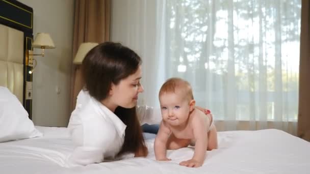 快乐的母性观念可爱的年轻妈妈抱着8个月大的女儿，用雪白的毛毯在舒适的卧室里哺乳。家庭的柔情和幸福。孩子，孩子，婴儿，孩子，宝贝。4k视频 — 图库视频影像