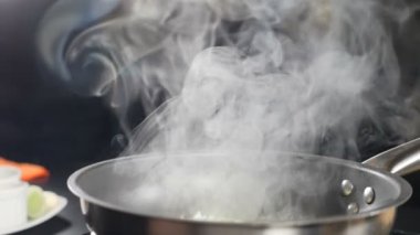 Beyaz duman ağır çekimde siyah arka planda kızgın tavanın üzerinde yükseliyor. Restoranda yemek pişirmek. Lokanta mutfağında pişirilen lezzetli risotto. Tam Hd