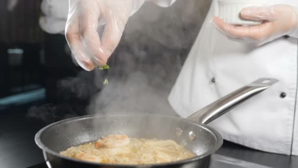 Chef cocinando deliciosos mariscos risotto en sartén. Disparo en cámara lenta. Chef añadiendo hierbas frescas en la sartén. Receta de la cocina tradicional italiana. risotto de camarones en gourmet — Vídeo de stock