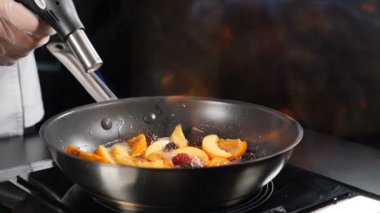 Meyveler tavada ateşle pişiriliyor. Lezzetli Flambe meyveli tatlı pişiriyorum. Işıklandırma Aşçı Fenerini Yavaş Çekimde.. Şef restoranda ateşle yemek pişiriyor. Tam Hd