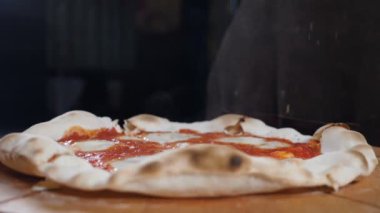 İtalyan restoranının mutfağında yavaş çekimde pişmiş hazır pizzanın üzerine baharat döken şefin yakın çekimi. Masada yeşillikle süslenmiş lezzetli bir pizza. Tam Hd