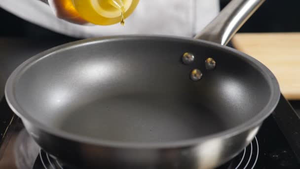 Warme koekenpan op het fornuis. Olie gieten in slow motion. Koken. Chef giet zonnebloemolie in koekenpan, macro shot. Olijfolie wordt gegoten. Vol hd — Stockvideo