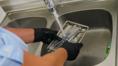 Diş kliniğinde sterilizasyon, bakteriyel arıtma ve dezenfeksiyon. Diş hekimi asistanı dişçi aletlerini musluktan akan suyun altında fırçayla yıkıyor. Yakın plan. 4k video