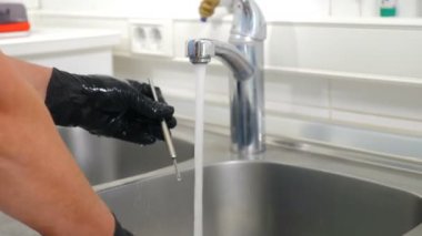 Diş kliniğinde sterilizasyon, bakteriyel arıtma ve dezenfeksiyon. Diş hekimi asistanı dişçi aletlerini musluktan akan suyun altında fırçayla yıkıyor. Yakın plan. 4k video