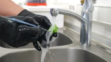 Diş kliniğinde sterilizasyon, bakteriyel arıtma ve dezenfeksiyon. Diş hekimi asistanı dişçi aletlerini musluktan akan suyun altında fırçayla yıkıyor. Yakın plan. 4k video