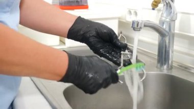 Diş kliniğinde sterilizasyon, bakteriyel arıtma ve dezenfeksiyon. Diş hekimi asistanı dişçi aletlerini musluktan akan suyun altında fırçayla yıkıyor. Yakın plan. 4k video
