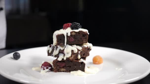 Stapel brownies dessert wordt versierd met bessen op een wit bord. Vallende Bessen in Slow Motion. Chocolade koken heerlijk dessert in restaurant keuken. Vol hd — Stockvideo