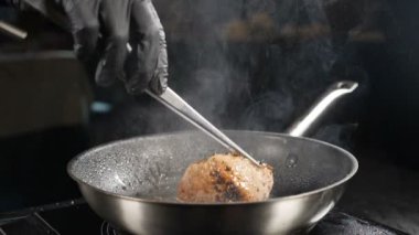 Restoranda yemek pişirmek. Güzel mutfak. Şef yavaş çekimde yemek maşasıyla eti çeviriyor. Yağ damlalarıyla tavada kızartılan sulu et. Kızarmış biftek ve dumanlı biftek. Tam Hd
