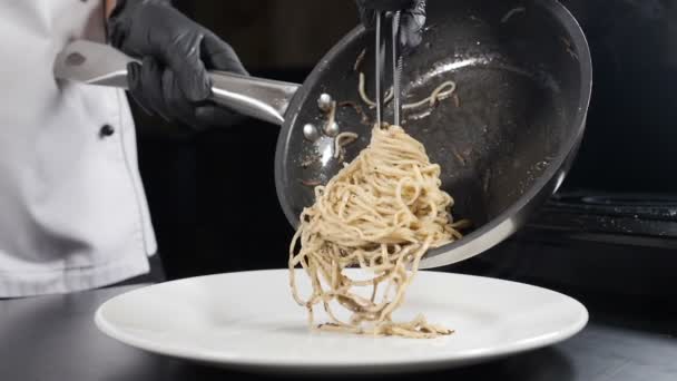 Chef sirviendo pasta en el plato. Poner espaguetis terminados con trufa en plato con pinzas, sirviendo plato italiano. Cocina en cafetería o restaurante. Vapor blanco subiendo en cámara lenta. Full hd — Vídeo de stock