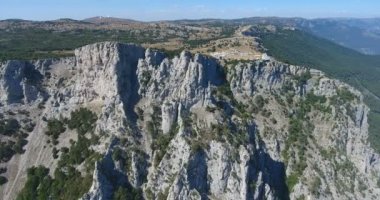 Kırım doğası, kayalar ve dağların havadan görünüşü. Büyük kayalıklara yakın uçuyor. Uçurumlar ve dağlarla kaplı Kırım manzarası. Uçurum yamacı ve dağ hattı. 4k video